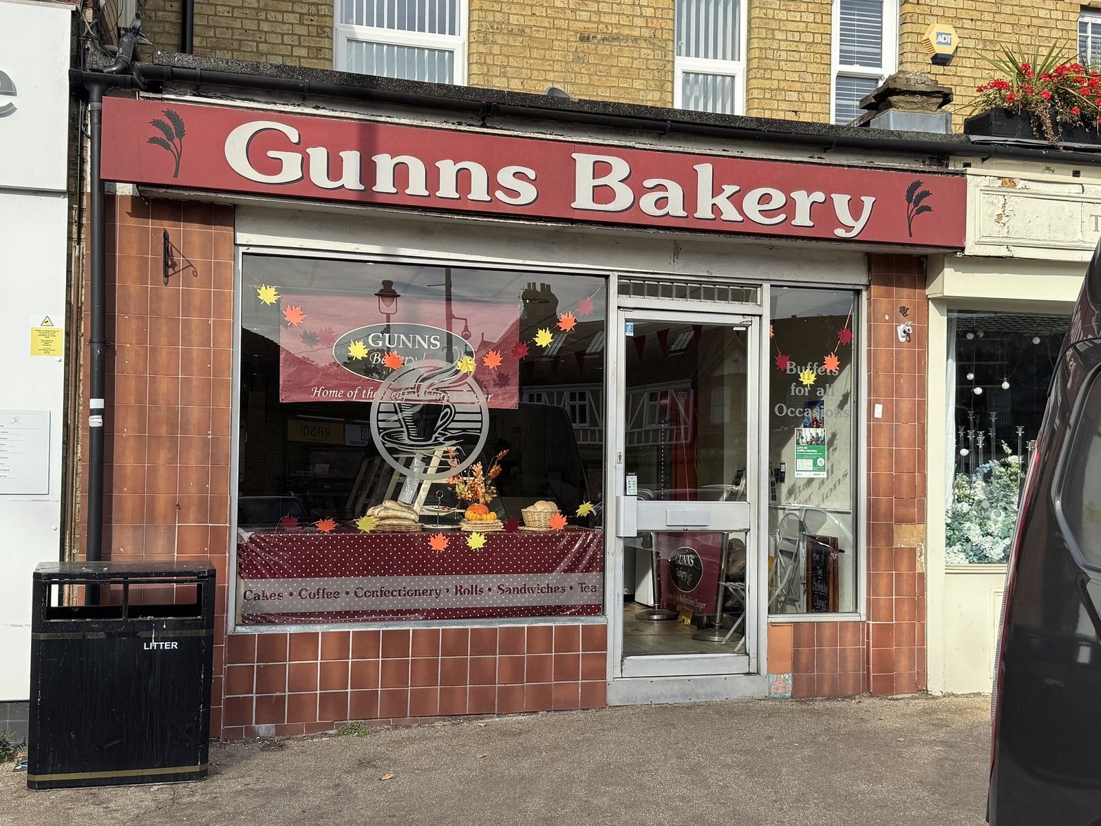 The shopfront of Gunns Bakery on Market Square, Sandy, with its red sign, tiled front and an autumn window display of bread and leaves